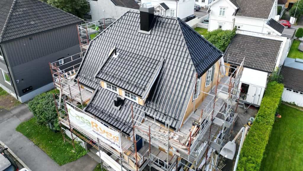 Enebolig med nytt tak og stillas rundt, omgitt av nabolag med hus og hager sett ovenfra.