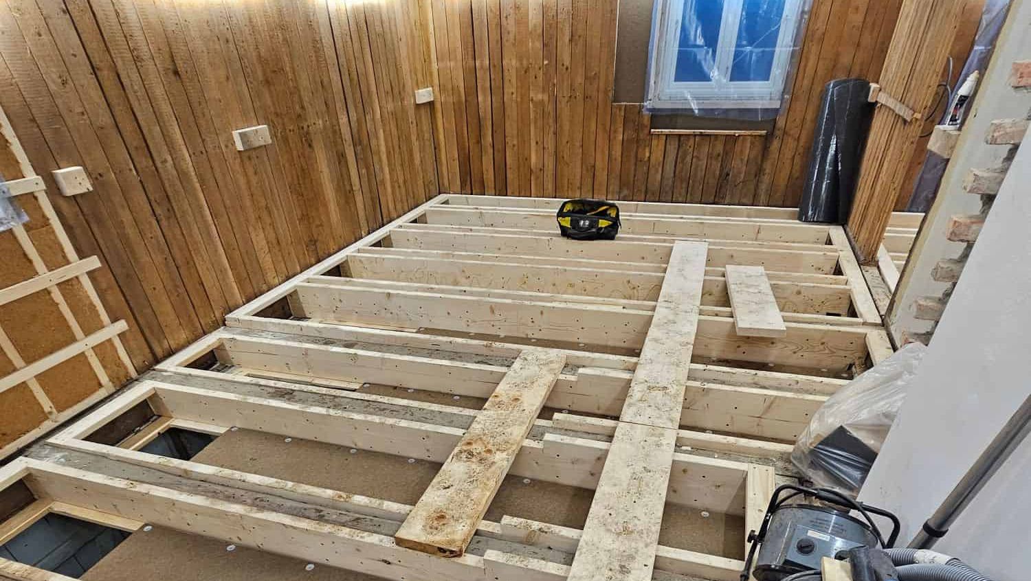 Bindingsverk til nytt gulv montert i rom med trepanel på vegger, klart for videre oppbygging.