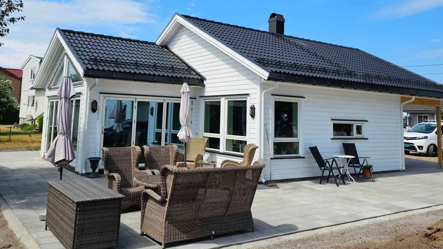 Ny enebolig med ferdig uteplass, moderne tak og hagemøbler plassert på steinbelagt terrasse.